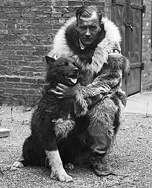 Photographie en noir et blanc d'un pilote d'attelage avec son chien de tête.