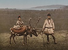 Dítě sedící na sobu, vpravo muž držící soba na uzdě. Oba v tradičním oblečení, s čepicemi.