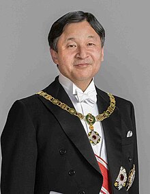 Wearing white tie and tails with sash and medals