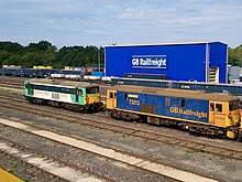 Two diesel locomotives, behind which is a large blue building with "GB Railfreight" on the side