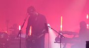 Three men playing drums, guitar and keyboards on stage in concert.