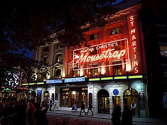 exterior of a London theatre at night, with large neon sign advertising The Mousetrap