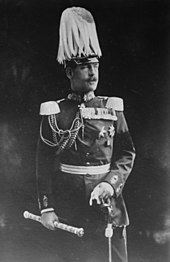 Photographie en noir et blanc : un homme moustachu en grand uniforme avec un casque à plumets et un bâton de maréchal.