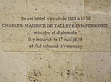 Photo d'un mur de grandes pierres blanches finement jointes, dont une au centre est gravée par les lignes suivantes : « En cet hôtel vécut de 1812 à 1838 / CHARLES-MAURICE DE TALLEYRAND-PERIGORD / ministre et diplomate / Il y mourut le 17 mai 1838 / et fut inhumé à Valençay ».