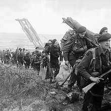 Black and white photograph of marines walking away from a beach in single file