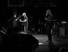 Three men onstage playing instruments and singing into a microphone