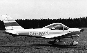 black and white side profile photograph of a PIK-19 Muhinu light aircraft on the ground with a person in the cockpit. the writing on the side of the aeroplane reads "OH-MHX"