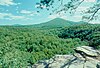 View from a flat rock across a forest to several wooded mountain peaks