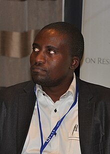 A seated Matengu at a table during an academic conference