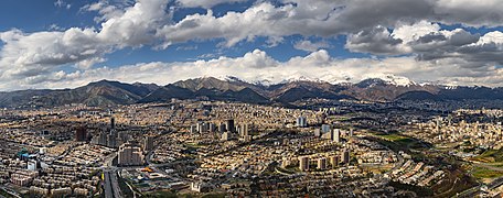 Devant de belles montagnes enneigées une grande ville, composée de quelques immeubles de grande hauteur, énormément de bâtiments, certains relativement bien rangés, d'autres s'accumulant sans ordre apparent, et quelques axes de circulation qui les traversent.