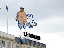 Visages de Tintin et Milou (tenant un os dans la gueule) au-dessus du toit d'un immeuble.