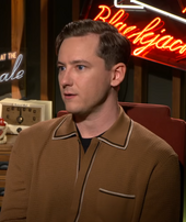 Lewis Pullman during an interview in 2018. A neon sign can be seen behind him.