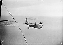 Photo en noir et blanc d'un hydravion quadrimoteur survolant des îles.