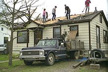 People working to clear debris off of a damaged home