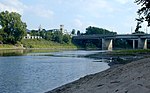 A middle-sized river with sandy and grassy banks flows under a bridge.