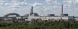 Usine grise avec, à gauche une structure en construction et, au milieu, plusieurs cheminées et des grues.