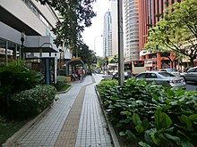 Photo of a sidewalk with small square tiles with a line of darker-colored long rectangular tiles in the middle