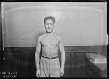 Photographie de presse en noir et blanc d'un homme musclé, torse nu, regardant l'objectif.