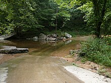 A color photograph depicting an improved ford across a small stream with a gravel road and lush foliage.