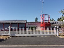 Photographie en couleurs d'un alignement de garages et d'un tourelle métallique peinte en rouge.