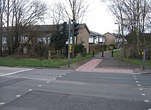 Photo of tactile paving where a bicycle path meets a road; the line where the path meets the road and a linear section going back onto the bike path form an L-shape