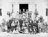 Family photograph of Pontians at a house. Some old women wear traditional clothes. A young boy holds a rifle.