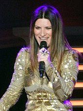 A woman holding a microphone up to his neck in a white dress with black.