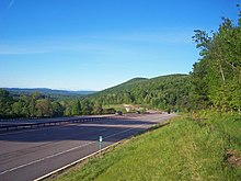 A divided highway curving across the bottom of the picture, passing a hill on the right in the foreground on its way to a more level landscape at left center