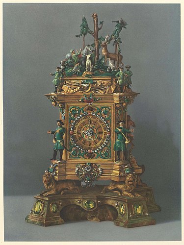 Stutzuhr mit emaillierten Figuren und reichem Juwelenschmuck. Auf dem Aufsatz die Legende des hl. Hubertus. Das Werk von J. G. Graupner in Dresden. Das Gehäus von Johann Christoph Köhler in Dresden für August den Starken gefertigt