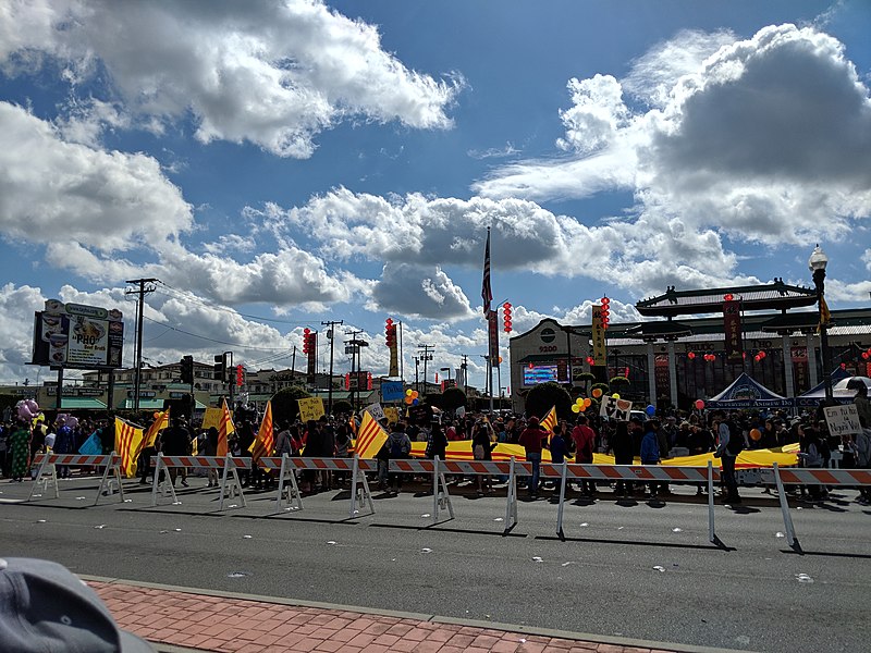 Vietnamese American youths with signs promoting Vietnamese language and culture ("I like to learn Vietnamese" and "I'm proud to be Vietnamese") at a parade.