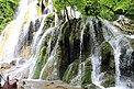 Fast das gesamte Foto ausfüllend ergießt sich gischtsprühend das Wasser des höchsten der Beușnița-Wasserfälle über einen Felsen. Im Hintergrund sind Bäume zu sehen.