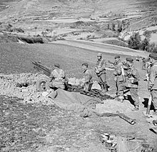 Six men around an artillery gun dug in with another gun in the distance