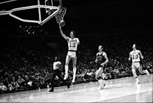 Joueur de basket-ball, sautant en l'air, tenant le ballon de sa main droite, pour le déposer dans le panier.