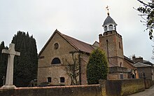 A small brick church surrounded by trees, with a war memorial en the foreground