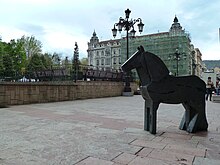 Photo représentant une statue de poney stylisé géométrique sur une place, un bâtiment ancien en travaux en arrière-plan.