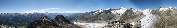 Panorama d'un glacier avec des moraines médianes serpentant dans une vallée entourée de montagnes.