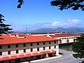 Photograph of docks and red-roofed, stucco warehouses at the San Francisco Port of Embarkation, U.S. Army. The Golden Gate Bridge spans the background of the picture.