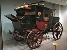 voiture hippomobile fermée, à 4 place et 4 roues, vue de 3/4 avant. On voit à gauche le siège du cocher, à droite le coffre du courrier