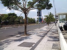 Photo of a sidewalk with a line where tiles have been replaced by a dark gray ridged area of pavement