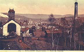 De gauche à droite : La recette du puits surmonté du chevalement en bois, à l'arrière plan, on aperçoit le chevalement en béton du puits sainte-Marie, en dessous de l'église on aperçoit le petit chevalement métallique du puits de secours, la cheminée du ventilateur et la cheminée des chaudières.