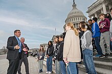 Two older white men in suits address a group of teenagers assembled on the steps of the U.S. Capitol