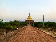 Down a dirt road is the gilded dome of the stupa, with a brick base.