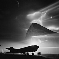 Un Douglas Dakota de la BOAC, en préparation pour un vol à destination du Royaume-Uni et éclairé dans la nuit de Gibraltar par les batteries de recherche lumineuses placées sur le rocher.