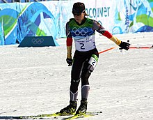 Photographie d'une biathlète faisant du ski de fond avec une combinaison noire, grise, jaune et rouge, portant le numéro 2, les bâtons vers l'arrière.