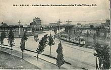 Photographie en noir et blanc de la bifurcation d'une vaste avenue bordée d'une allée cavalière plantée de jeunes arbres, avec un tramway et une voiture à cheval