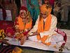 A Hindu wedding ritual in progress. The bride and the groom are seated together, receiving instructions from the priest.