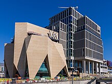 Shells of two buildings under construction by cranes. One is composed of rectangular blocks, the other is more angular