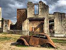 Photographie en couleurs de la carcasse d'une Peugeot 202 au milieu des ruines