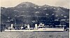 A white-painted warship at anchor in front of a large hill studded with buildings