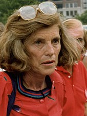 Eunice Kennedy Shriver hat blondes halblanges Haar und trägt ein rotes Oberteil.